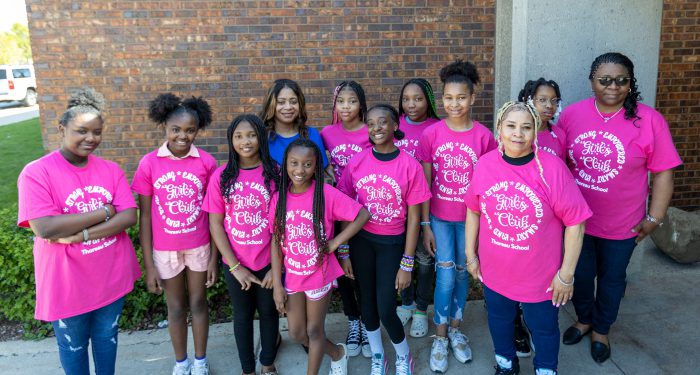 Members of the Thoreau School girl's club pose in front of the school wearing matching pink shirts.