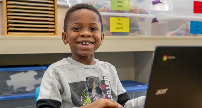 A young child smiling while using a computer.