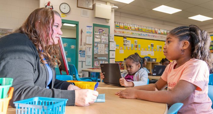 A teacher at a table talking to a young child.