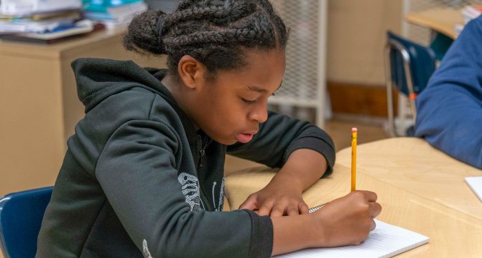 A student at a table writing in a notebook.