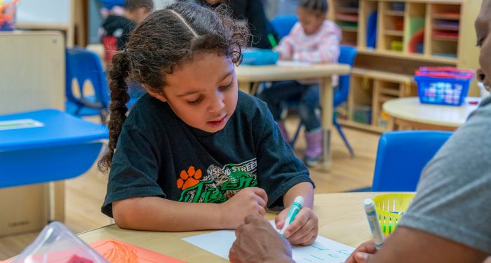 A young student traces her name on a piece of paper.
