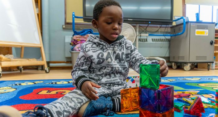 A young boy sits on a colorful rug and makes blocks from magnetic tiles.