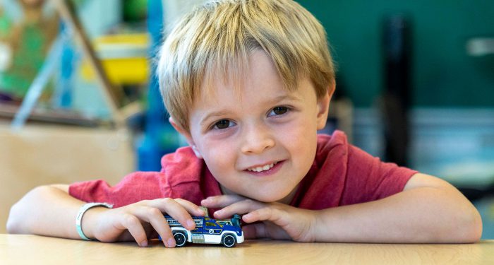 A young student playing with a toy car on a table.