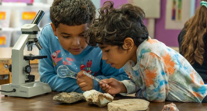Two students examine rocks with small magnifying glasses.