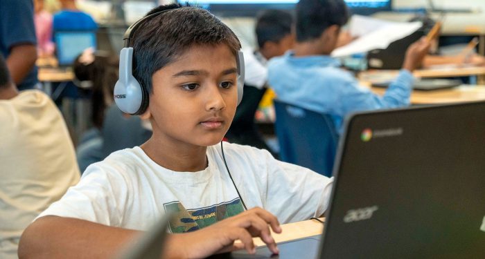 A student with headphones uses a laptop.