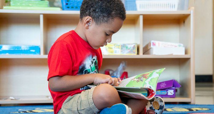 A young child sitting on the floor looking at a picture book.