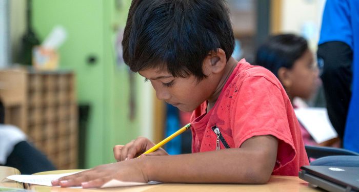 A young student at a desk writing on a piece of paper.