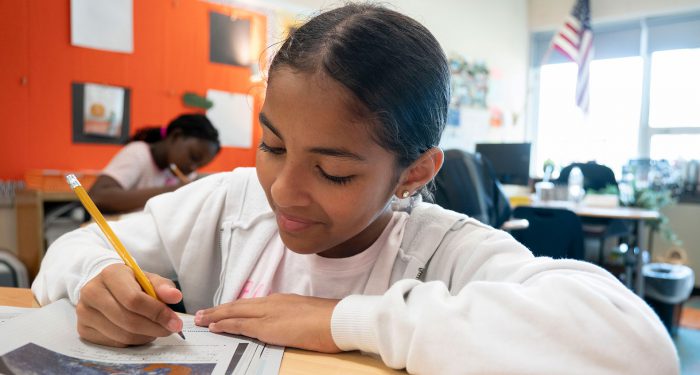 A girl in a classroom writing in a workbook.