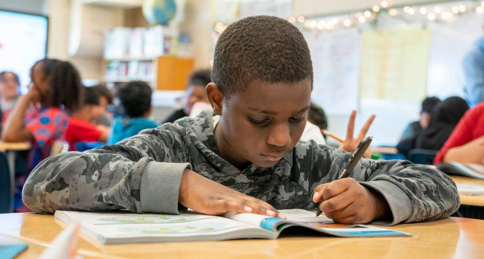 A student in a classroom writing in a notebook.