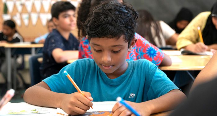 A student in a classroom writing in a notebook.