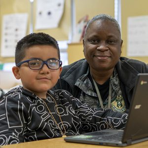 A student works on a computer while his teacher watches