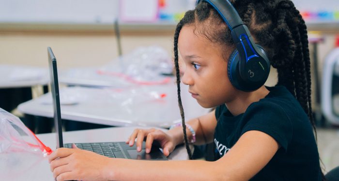 A young student wears headphones while they use a laptop computer.