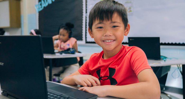 A student in front of a computer, smiling.