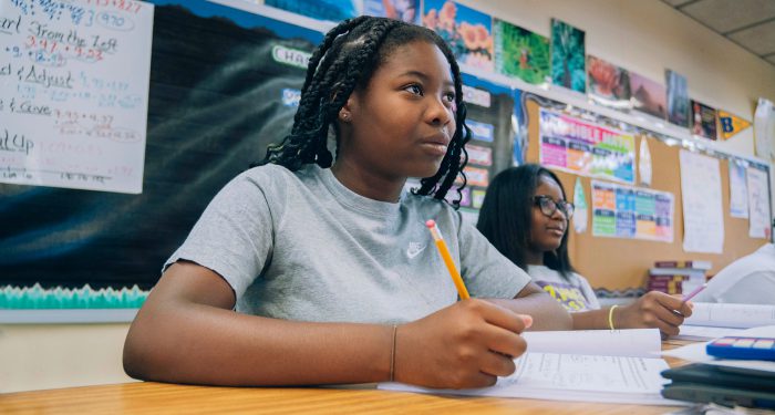 Students in a classroom look to the front of the room.