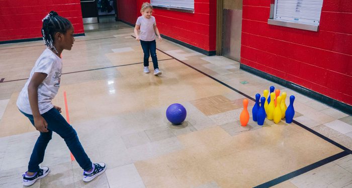 Young children play a bowling game in a gymnasium.