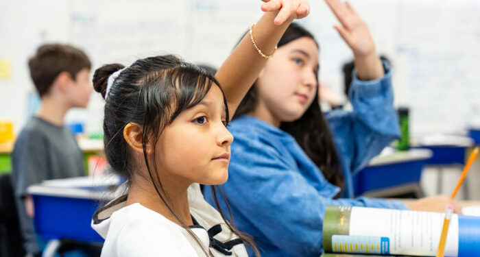Children in a classroom raising their hands.