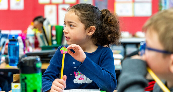 A young child in a classroom with a cupcake pencil topper.