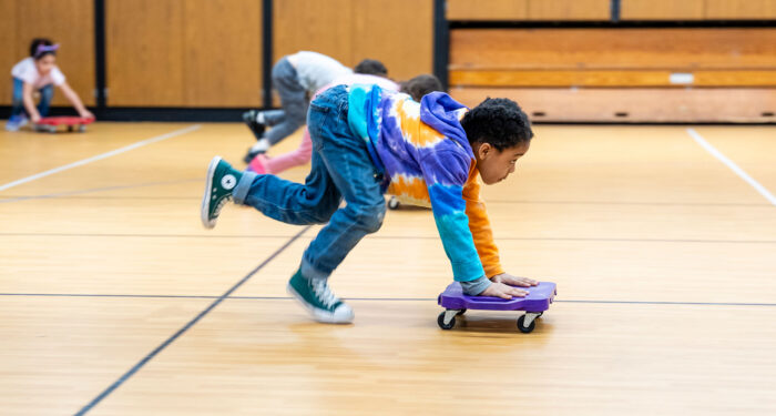 Young students in a gymnasium using scooter boards.