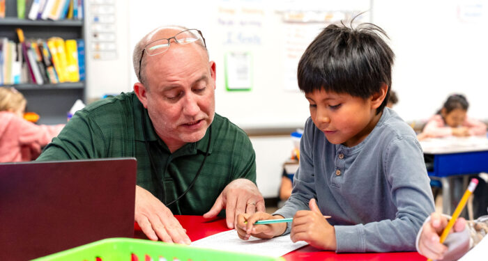 A teacher in a classroom helping a young student.
