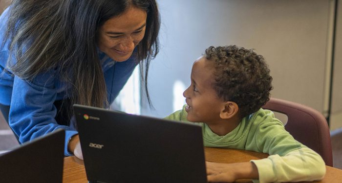 A teacher looks at the computer screen of a young student.